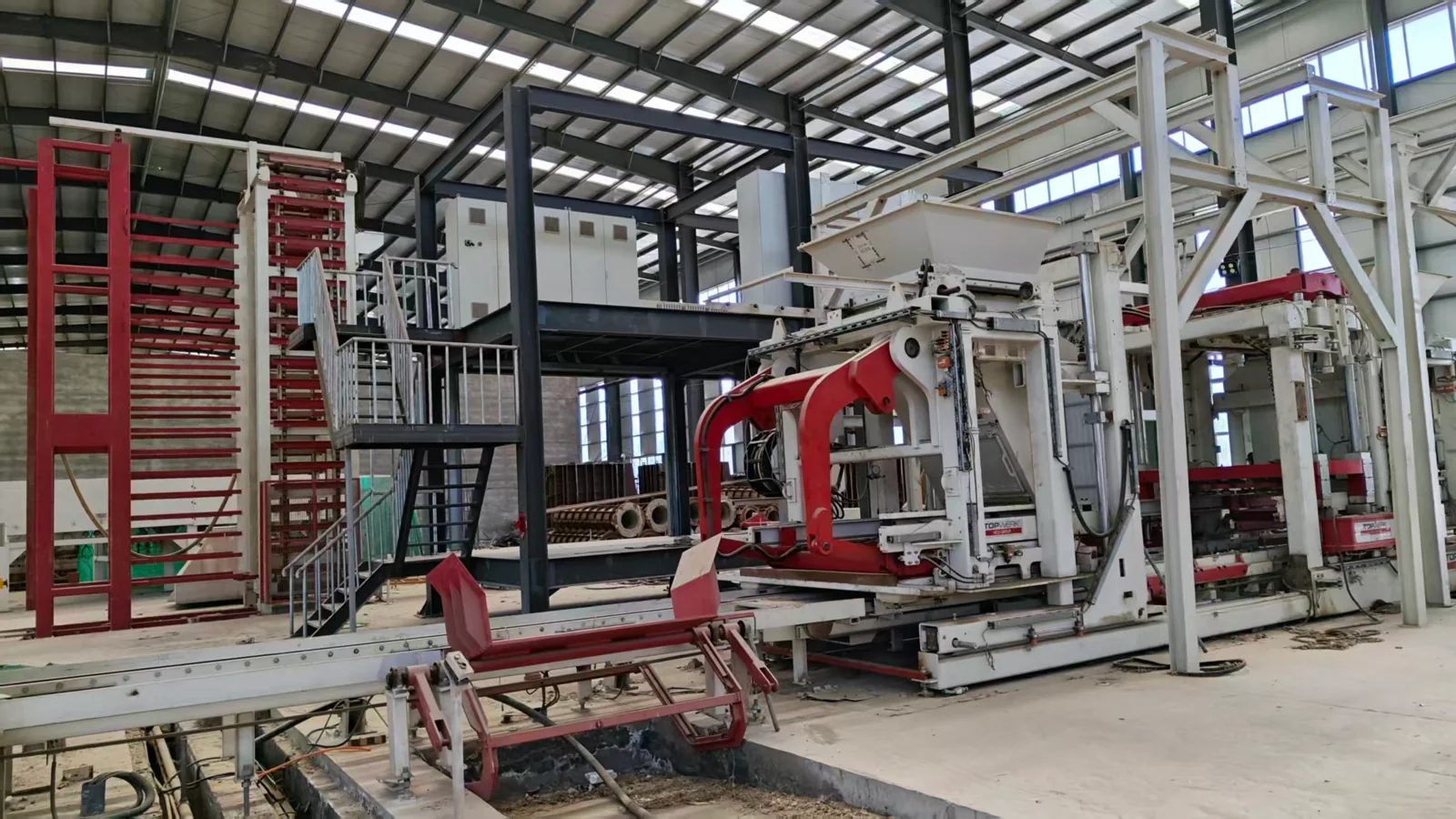 Used concrete block equipment with a red handling system and white machine frame inside a workshop